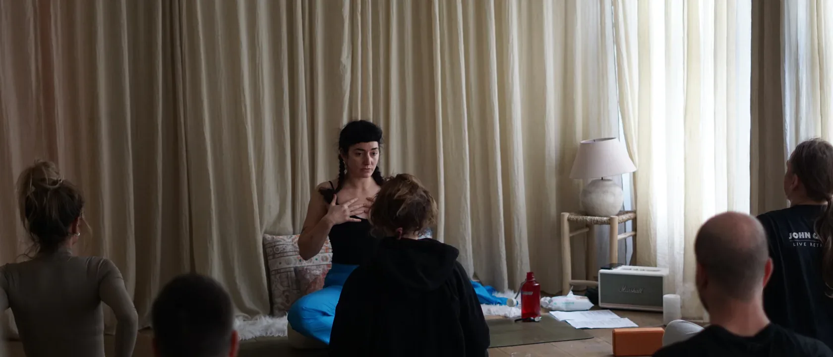 Ioanna underviser et siddende yogahold i et studie
